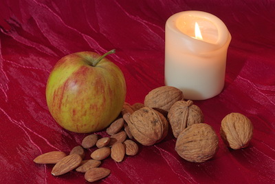 Apfel, Kerze, Nüsse un Mandeln auf roter Samtdecke