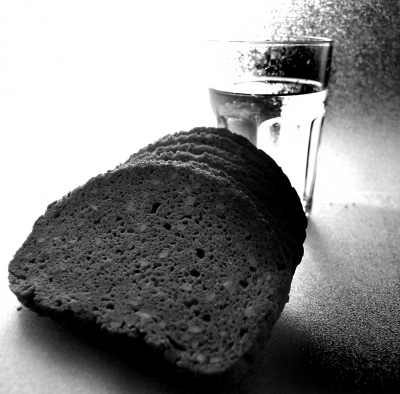 Glas Wasser und Scheiben von Schwarzbrot in Schwarz-Weiss