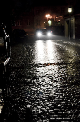 Nasse gepflasterte Strasse bei Nacht mit Auto im Hintergrund