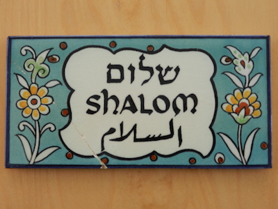 Wandfliese mit Blumen und dem hebräischen-lateinischen-arabischenSchriftzug Shalom-Salam