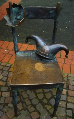 Bronzener Stuhl mit Krone und Narrenkappe