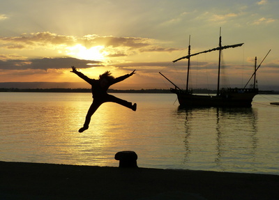 Freudenhochspringende Person im Sonnenuntergang an einer Kaimauer
