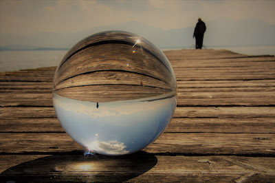 Person auf einem Steg, gespiegelt in einer Glaskugel Person auf einem Steg, gespiegelt in einer Glaskugel