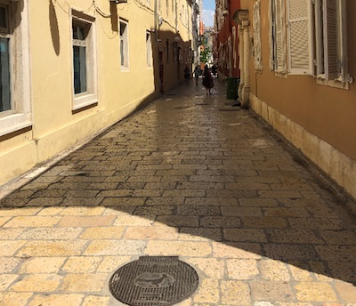 Blick in einen Strasse mit Gullideckel im Vordergrund