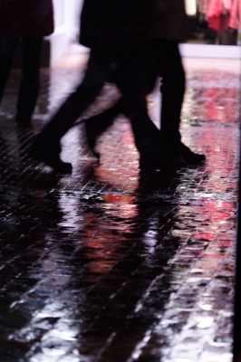 Beine, die abends auf nasser Pflasterstrasse unterwegs sind