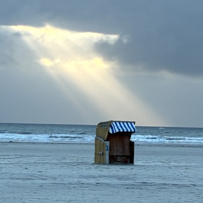 Strandkorb mit aus Wolken brechenden Sonnenstrahlen